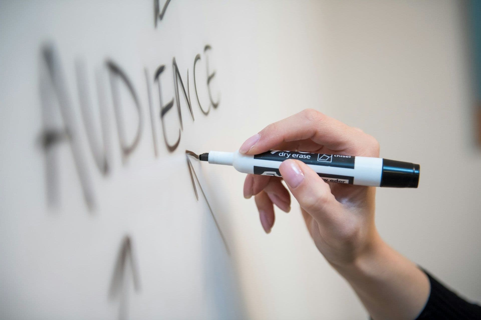 An image of female hand drawing the word audience on the whiteboard